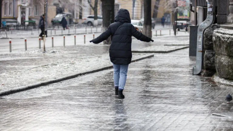 Женщина в пуховике скользит по скользкой от заморозков улице Киева.