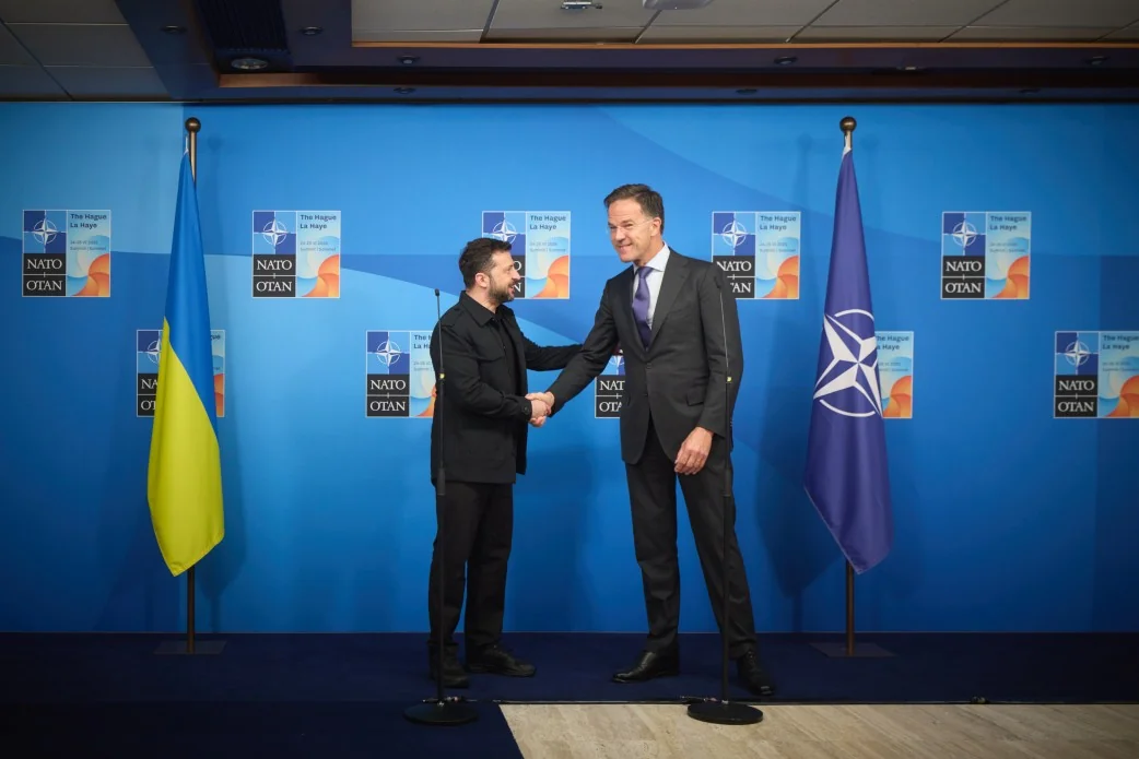 Володимир Зеленський тисне руку Єнсу Столтенбергу на тлі прапорів НАТО та України