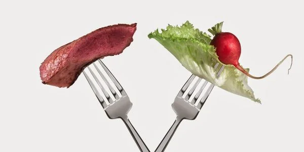 Дві виделки з мясом і овочами, що ілюструють вибір між мясоїдством та вегетаріанством