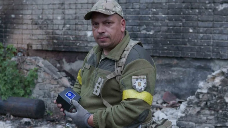 Військовослужбовець Нацгвардії України тримає пристрій на тлі зруйнованої стіни