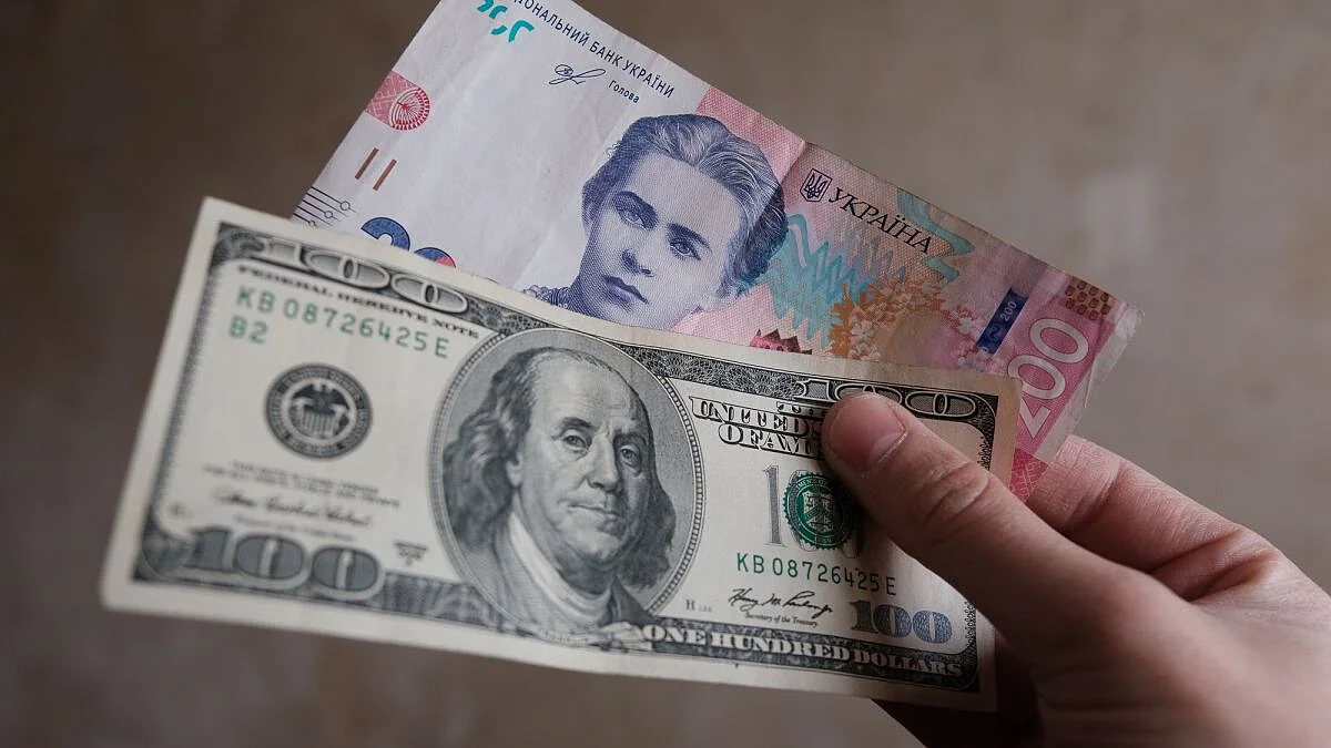 Рука тримає 100-доларову банкноту та купюру в 100 гривень