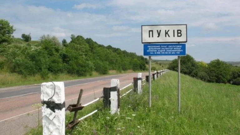 Дорожній знак села Пуків на узбіччі серед зелених пагорбів