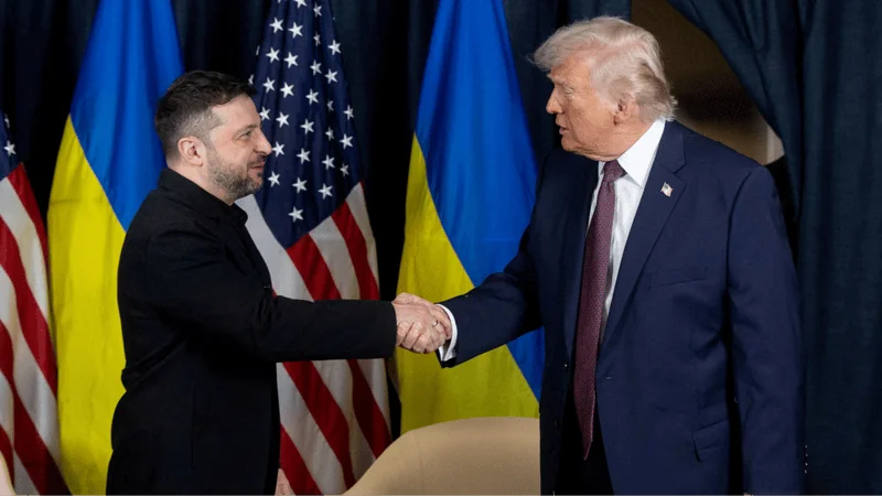 Владимир Зеленский и Дональд Трамп пожимают руки на фоне флагов Украины и США