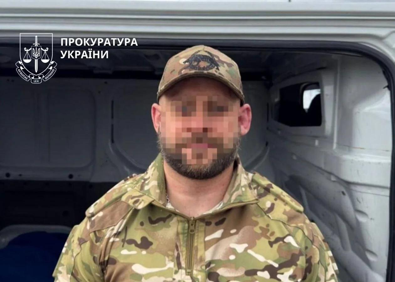Чоловік у камуфляжі з пікселізованим обличчям біля відкритого білого фургона