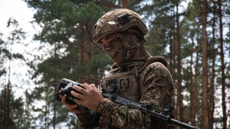 Військовий у шоломі та камуфляжі керує дроном у сосновому лісі