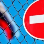 Червоний знак заборони в’їзду за сіткою на тлі розмитого прапора Росії