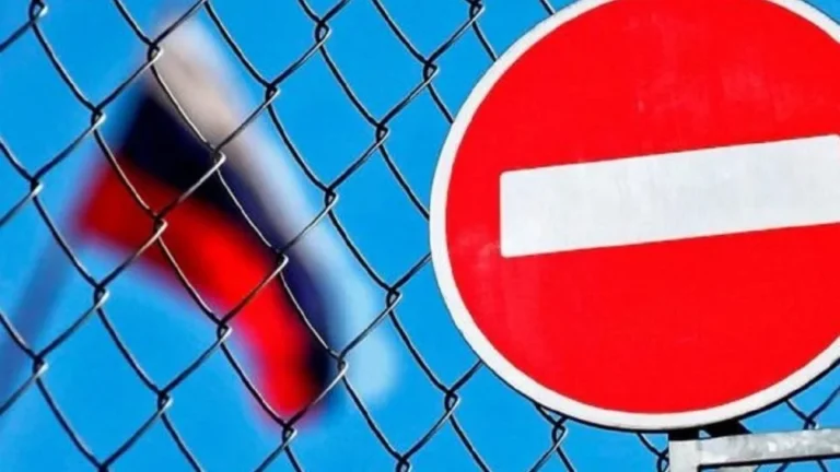 Червоний знак заборони в’їзду за сіткою на тлі розмитого прапора Росії