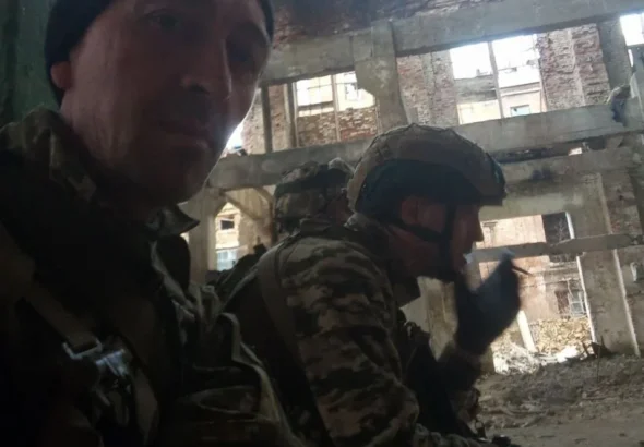Військовий у чорній шапці на селфі з побратимами в зруйнованій будівлі