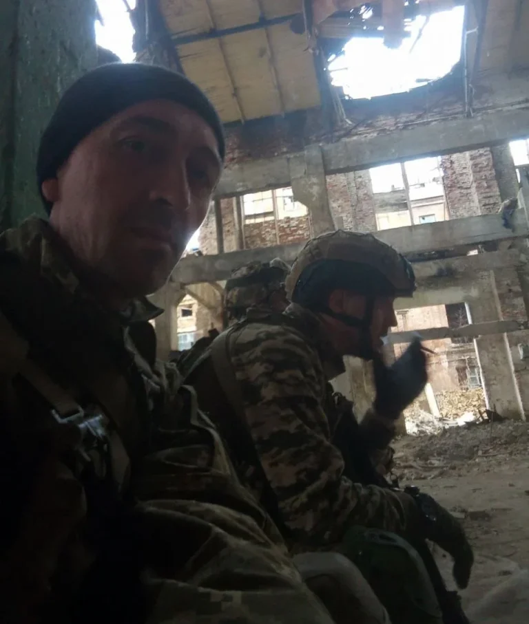 Військовий у чорній шапці на селфі з побратимами в зруйнованій будівлі