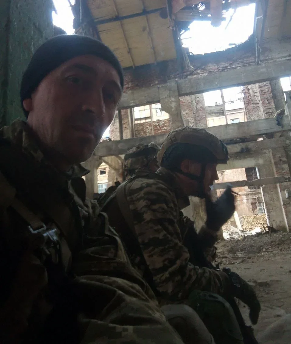 Військовий у чорній шапці на селфі з побратимами в зруйнованій будівлі