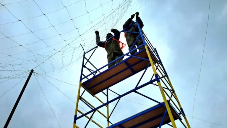 Двоє працівників на риштуваннях кріплять захисну сітку від дронів