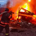Рятувальник у касці гасить сильну пожежу на палаючій техніці серед уламків