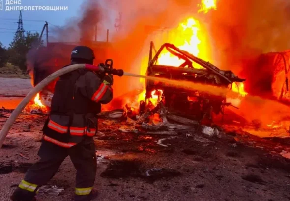 Рятувальник у касці гасить сильну пожежу на палаючій техніці серед уламків