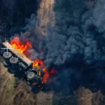 Палаючий багатоколісний військовий автомобіль на ґрунтовій дорозі серед густого диму
