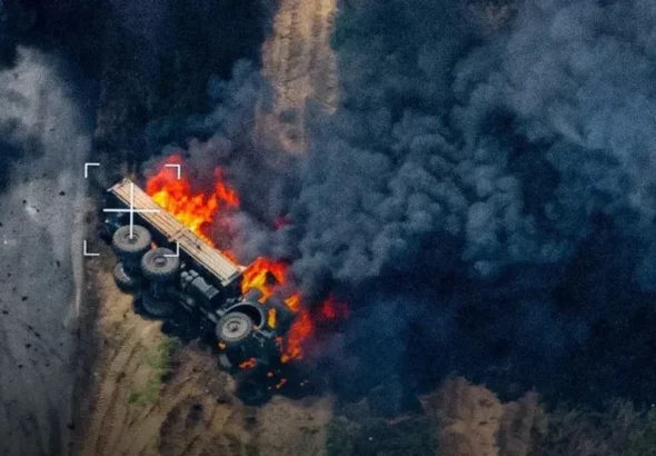 Палаючий багатоколісний військовий автомобіль на ґрунтовій дорозі серед густого диму