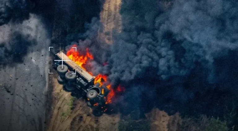 Палаючий багатоколісний військовий автомобіль на ґрунтовій дорозі серед густого диму