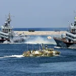 Два сірі військові кораблі та камуфляжний катер біля хвилелому в морі