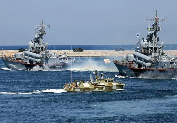 Два сірі військові кораблі та камуфляжний катер біля хвилелому в морі