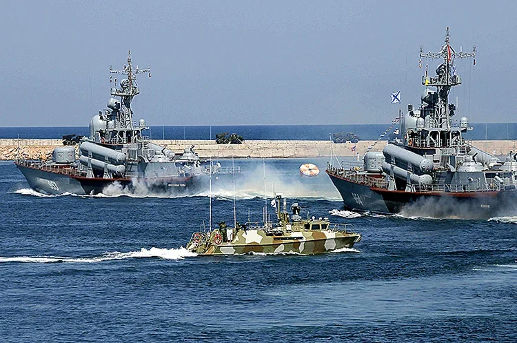 Два сірі військові кораблі та камуфляжний катер біля хвилелому в морі