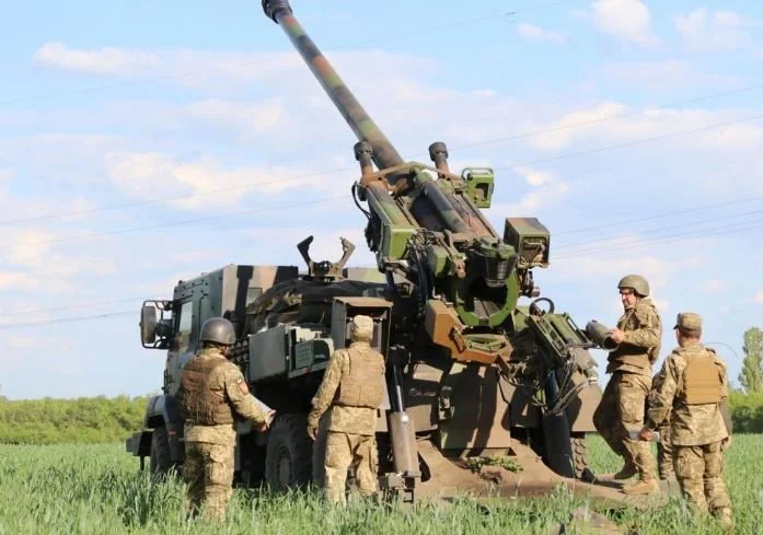 Українські військові біля самохідної гаубиці на зеленому полі під небом